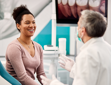 Woman in dental chair smiling while talking to her dentist