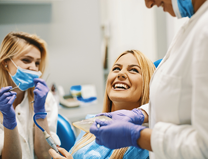 Woman in dental chair grinning up at her dentist