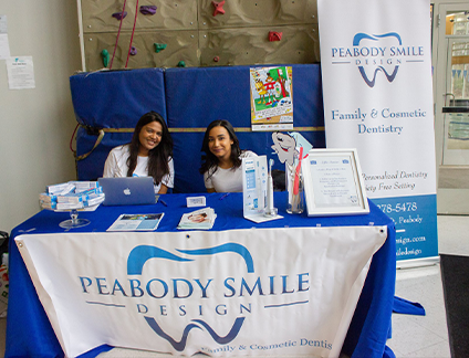 Two dental team members sitting at Peabody Smile Design table at local event