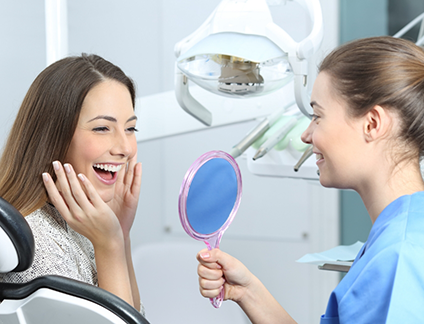 Woman in dental chair beaming while looking in a mirror