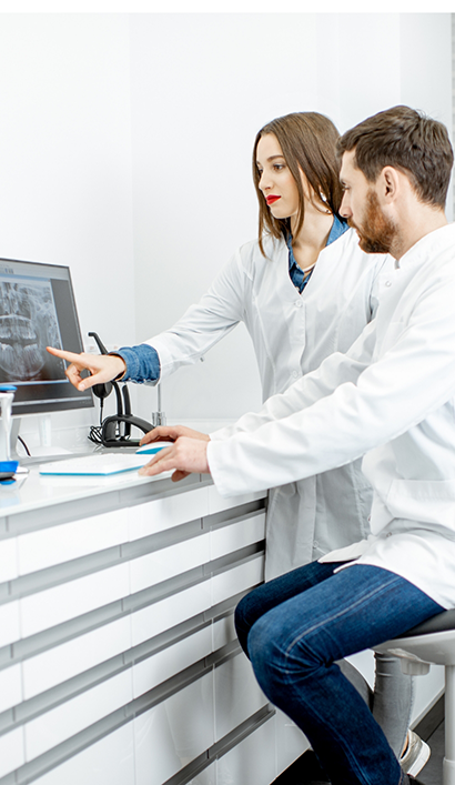 Two dentists looking at a computer screen showing x rays of teeth