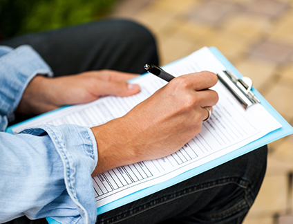 Person filling out paperwork on a clipboard