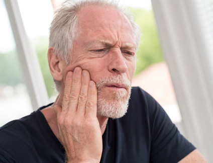 Man in black shirt rubbing jaw in pain