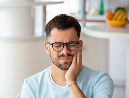 Man with glasses rubbing jaw in pain