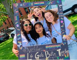 Four women taking selfie with giant picture frame covered in Pride flags