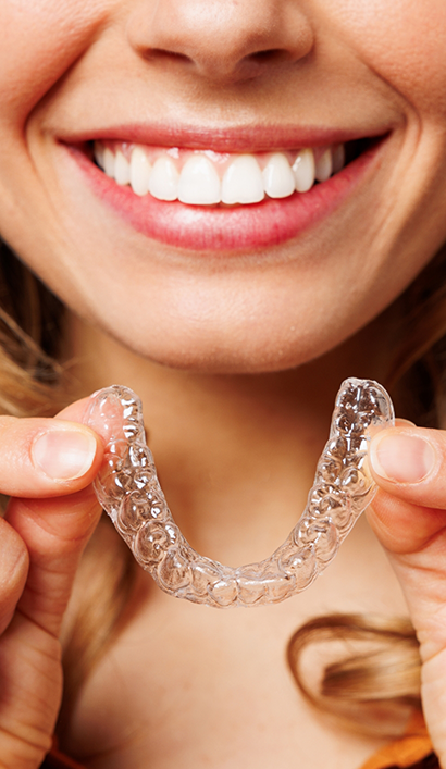 Smiling person holding an Invisalign clear aligner near their mouth