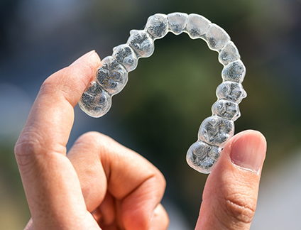 Close up of a hand holding an Invisalign aligner