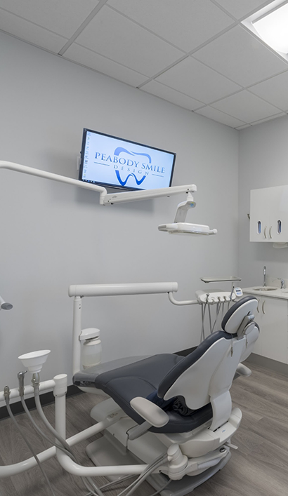 Dental treatment room with Peabody Smile Design logo on screen of T v mounted to wall