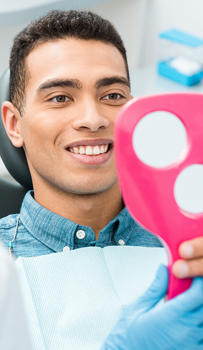 Man looking at his smile in a mirror after a preventive dentistry checkup