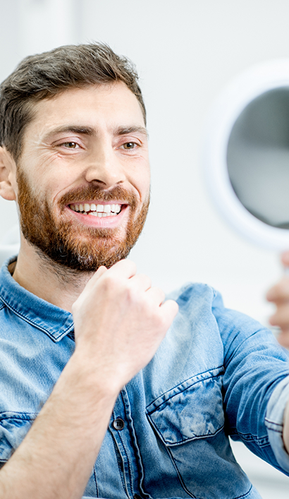 Man looking at his new smile in a mirror after restorative dentistry