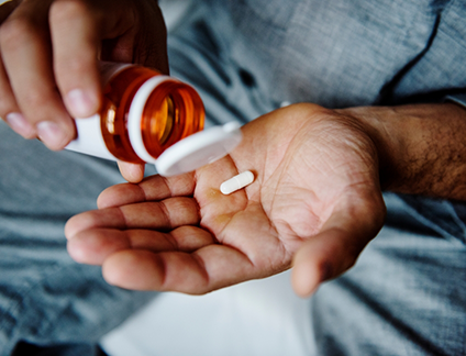 Person pouring a pill out of an orange bottle and into their hand