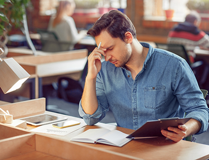 Man sitting at office desk pinching the bridge of his nose in frustration